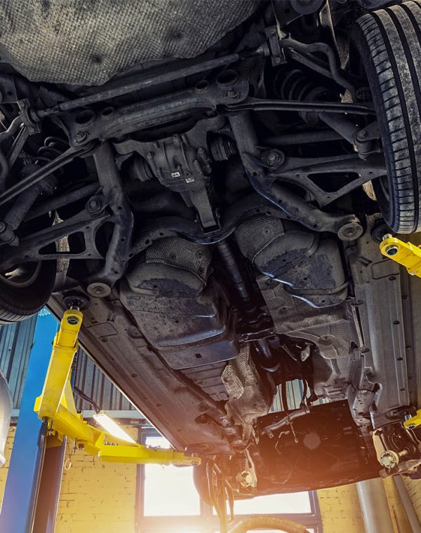 Bottom POV big modern SUV car with removed gearbox raised on lift elevator at workshop service maintenance station center. Vehicle check-up and repair. Underbody chassis and suspension parts
