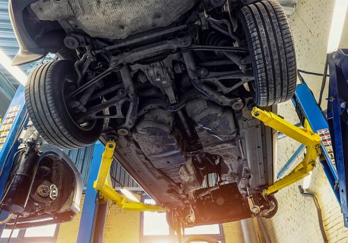 Bottom POV big modern SUV car with removed gearbox raised on lift elevator at workshop service maintenance station center. Vehicle check-up and repair. Underbody chassis and suspension parts
